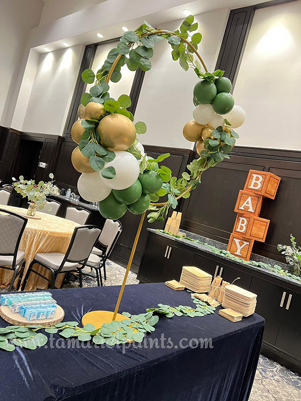 A photo of an artistic, circular balloon display with green, white and gold balloons on a table at an event